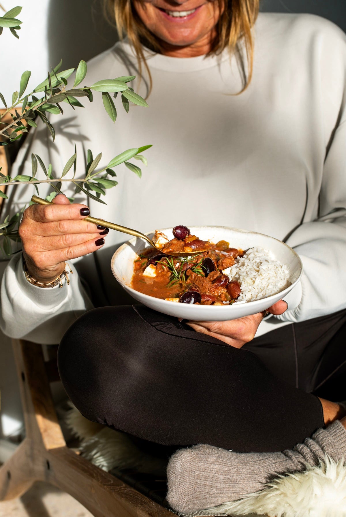 Frau sitzt mit einer Schale Rindergulasch und Reis auf dem Schoß und isst